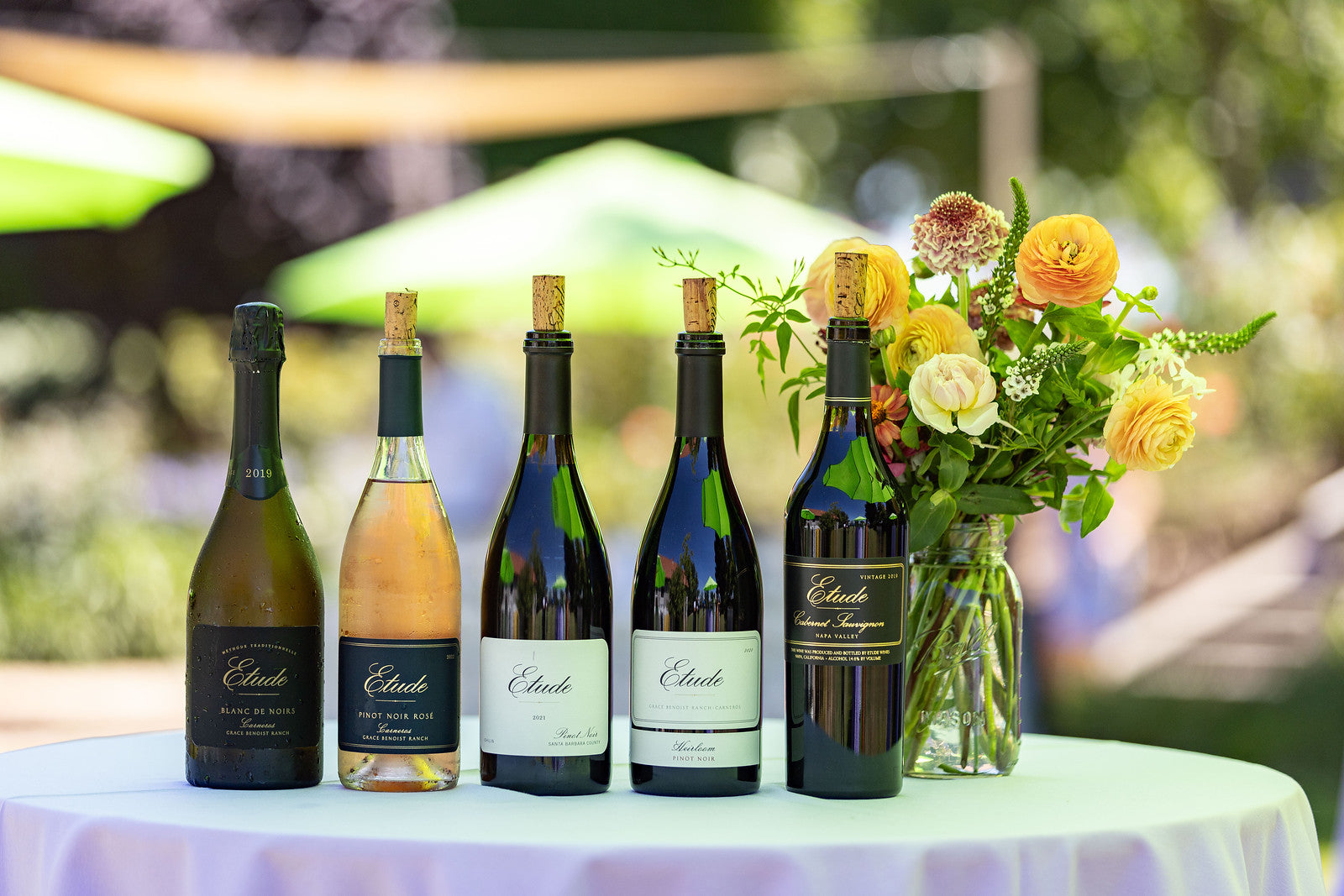 Etude wine bottles, including Blanc de Noirs, Pinot Noir Rosé, Pinot Noir, & Cabernet Sauvignon, with flowers on a white tablecloth.