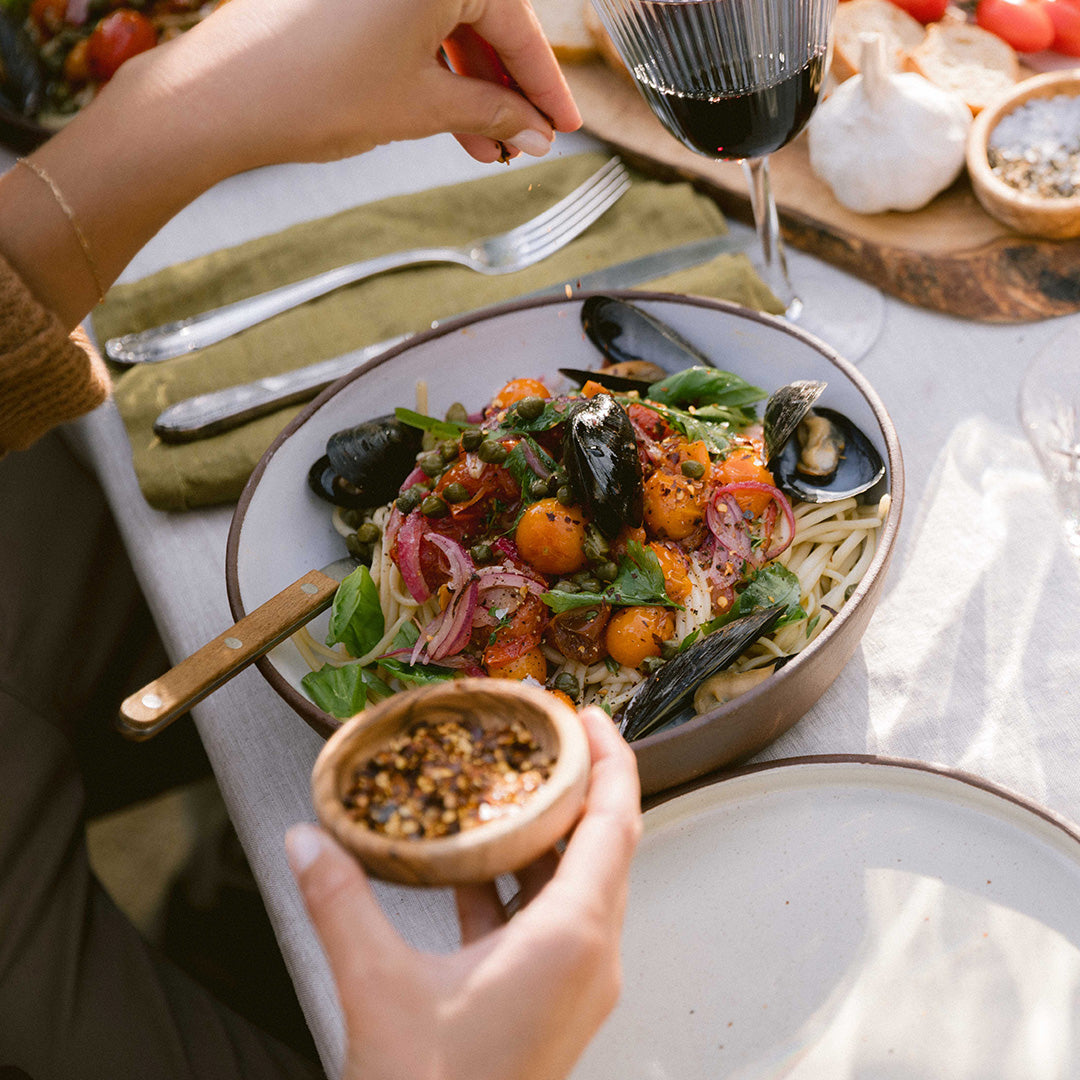 Person seasoning delicious pasta with mussels and cherry tomatoes.