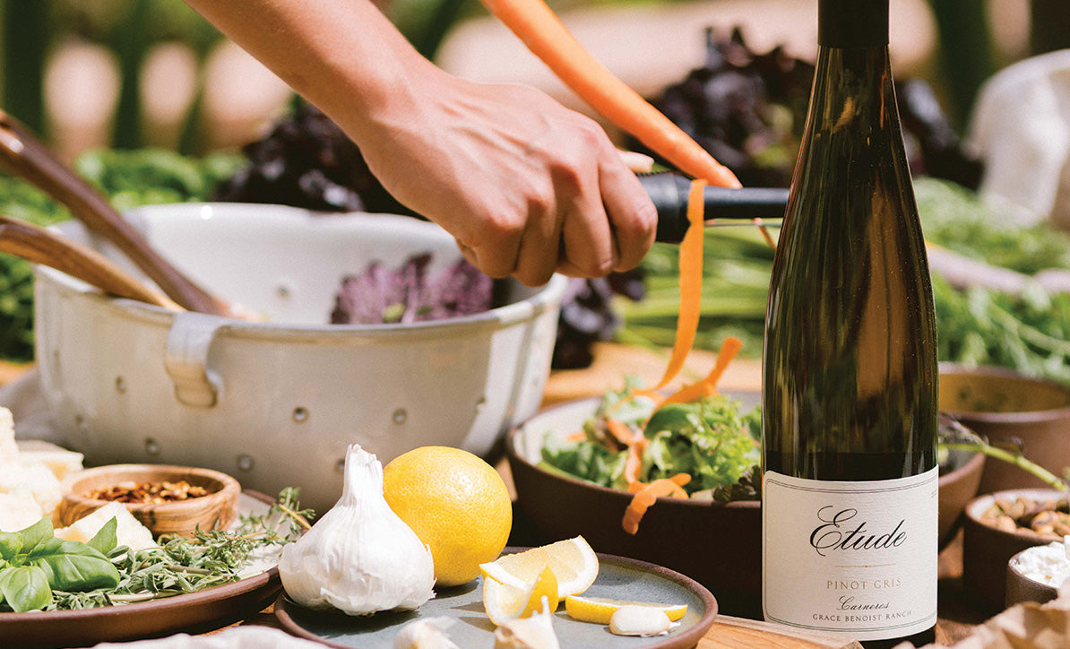 Person preparing a meal with Etude Pinot Gris wine and fresh vegetables.