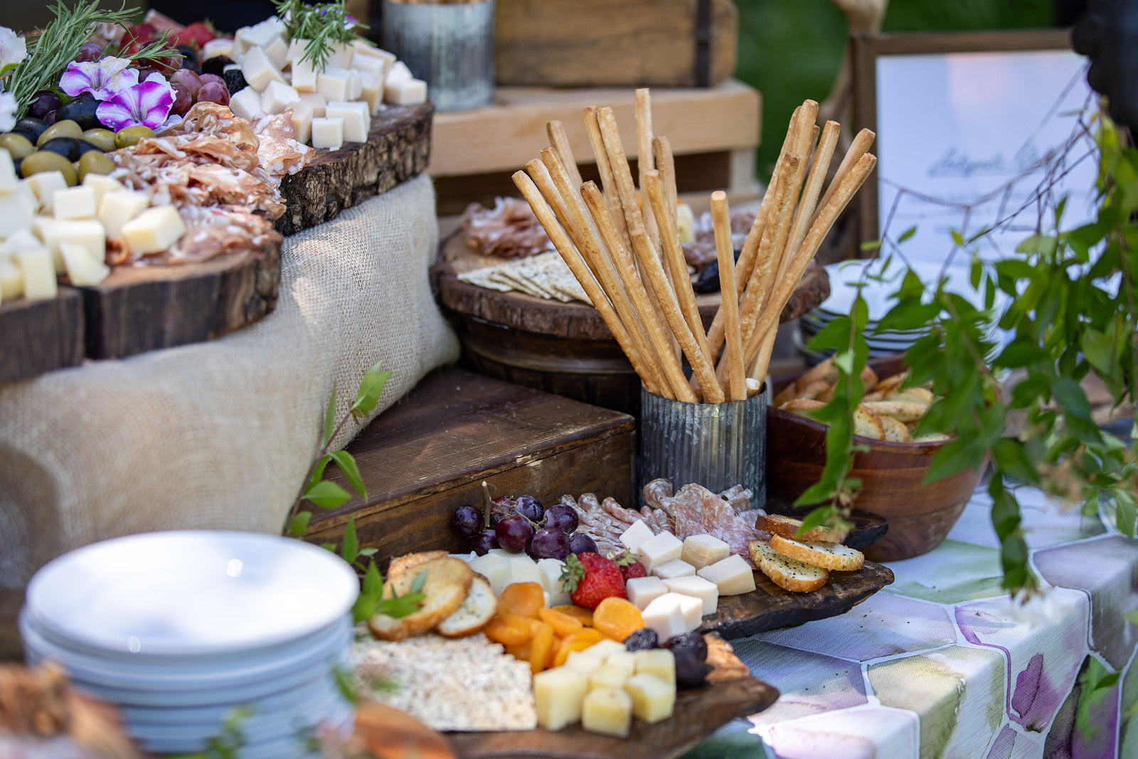 Rustic wooden boards laden with cheeses, meats, fruits, and breadsticks for a catered event.