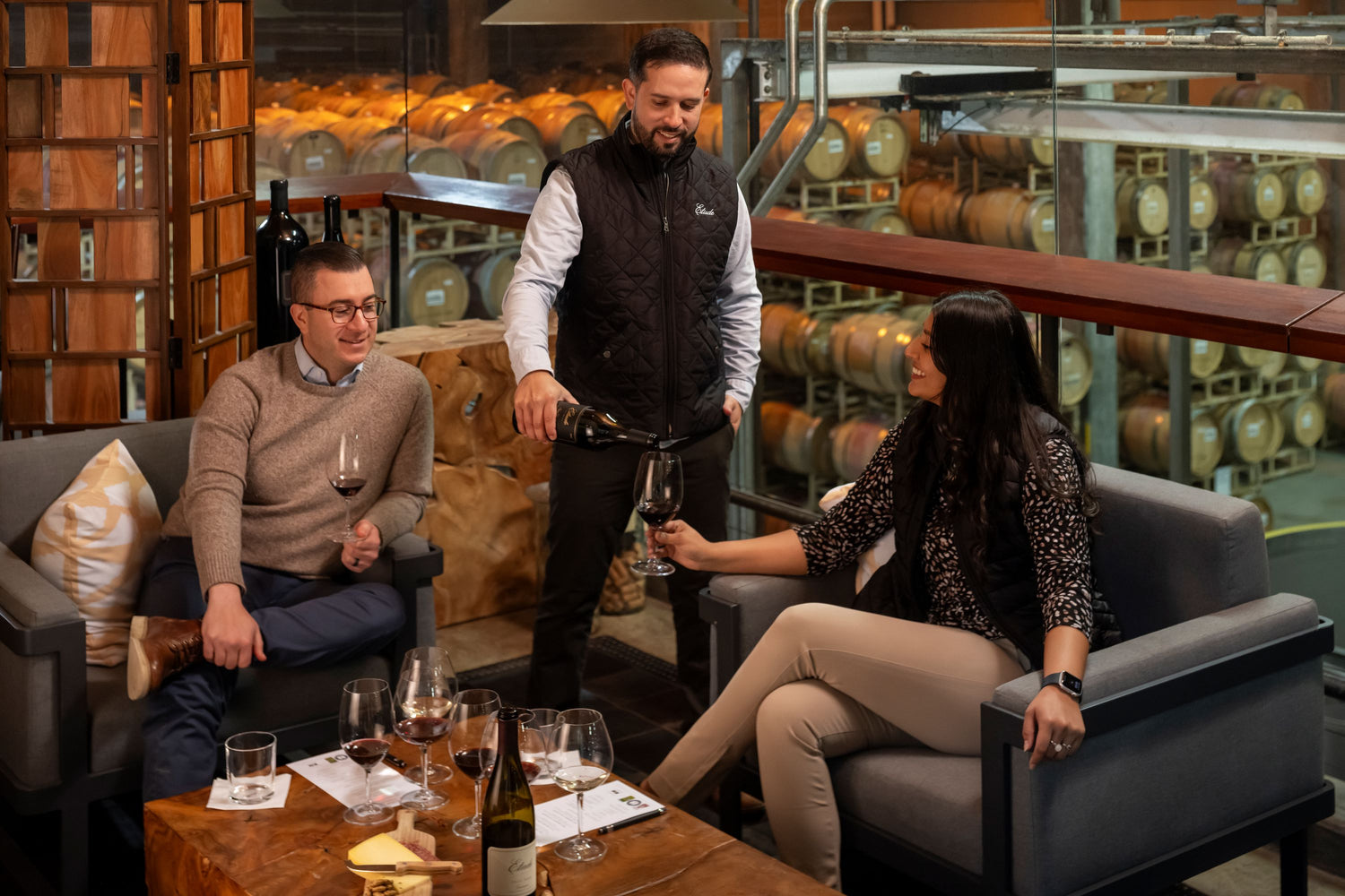People sitting in a wine cellar with wine bottles and glasses on a table.