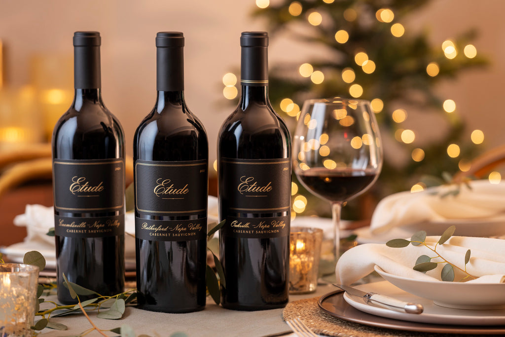 Three bottles of Napa Valley Etude Cabernet Sauvignon wine on a table with a festive background