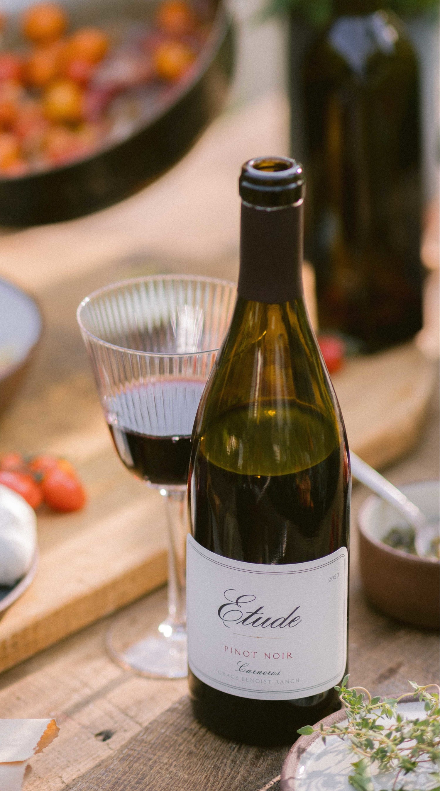 Bottle of Etude Pinot Noir Carneros wine on wooden table with wine glass and food