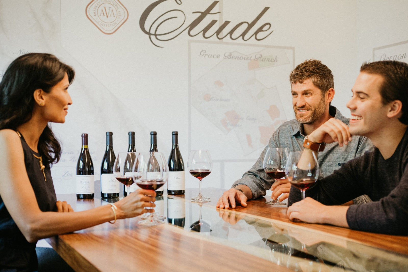 Three friends enjoying a wine tasting at Etude, examining bottles and glasses of red wine.
