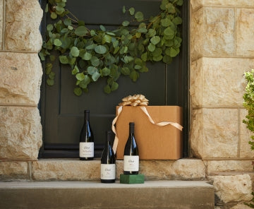 Three bottles of wine and a gift box on a doorstep.