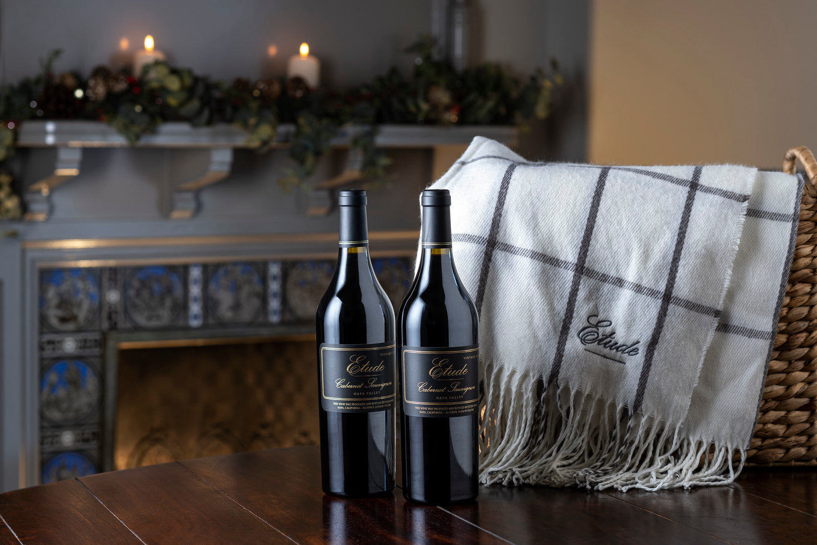 Two bottles of Etude Cabernet Sauvignon wine nestled in a cozy blanket near a fireplace.