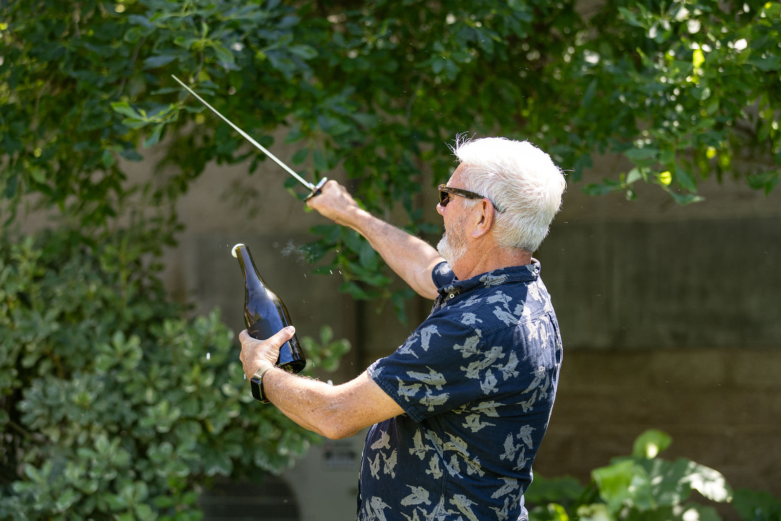 Winemaker Jon Priest sabering a bottle of champagne outdoors